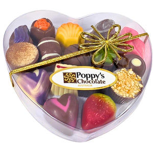 A heart-shaped clear gift box containing an assortment of gourmet chocolates, tied with a Gold ribbon and branded with 'Poppy's Chocolate'.