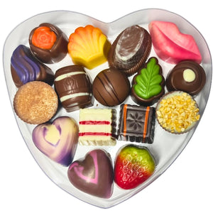 A heart-shaped clear gift box containing an assortment of gourmet chocolates, tied with a Gold ribbon and branded with 'Poppy's Chocolate'.