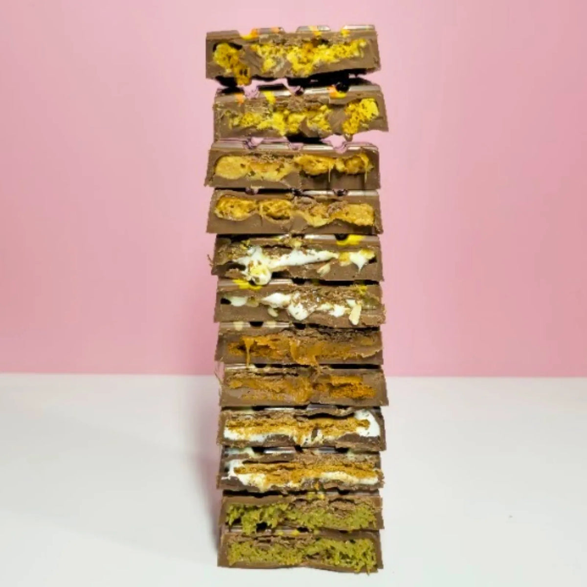 Stack of layered dessert bars with different textures on a pink background