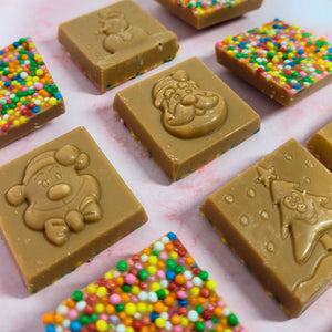 Close-up of caramel chocolate Christmas squares showing festive designs and colourful sprinkles.