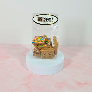Clear gift bag of caramel chocolate Christmas sprinkle squares displayed on a white stand.
