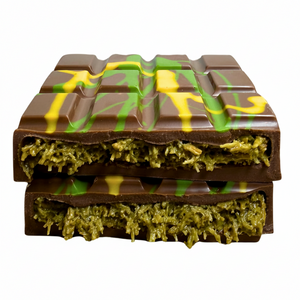 A pistachio and kataifi Bliss Block broken in half and stacked with a green textured filling and yellow drizzle, photographed on a plain white background.