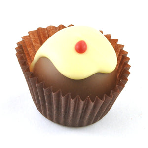 A delightful truffle from Poppy's Chocolate Christmas truffles 4 chocolate gift box appears in a brown paper cup, featuring a smooth milk chocolate ganache, topped with a layer of white chocolate and adorned with a tiny red dot.