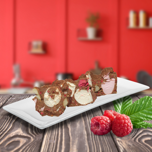 Sliced Rocky road featuring milk chocolate and raspberry sits elegantly on a white plate, resting on a wooden surface against a blurred red kitchen backdrop.