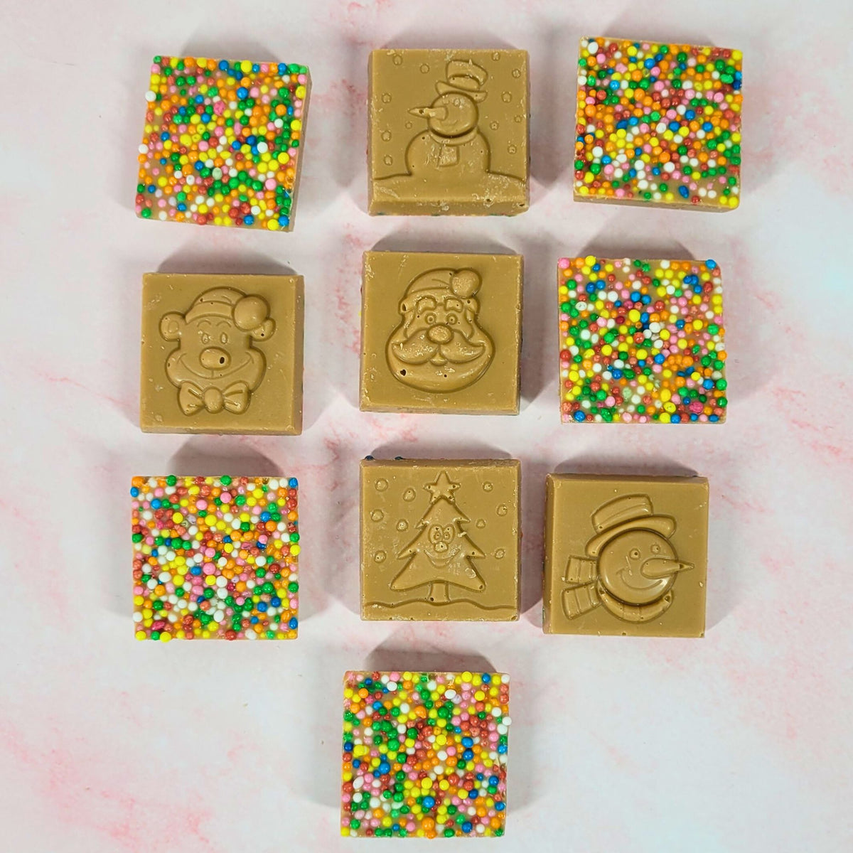 Ten caramel chocolate Christmas squares arranged to show festive moulded designs and colourful sprinkle-covered backs.