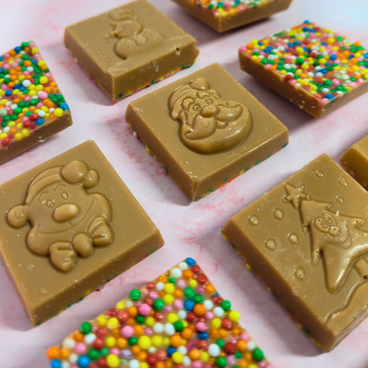 Close-up of caramel chocolate Christmas squares showing festive designs and colourful sprinkles.