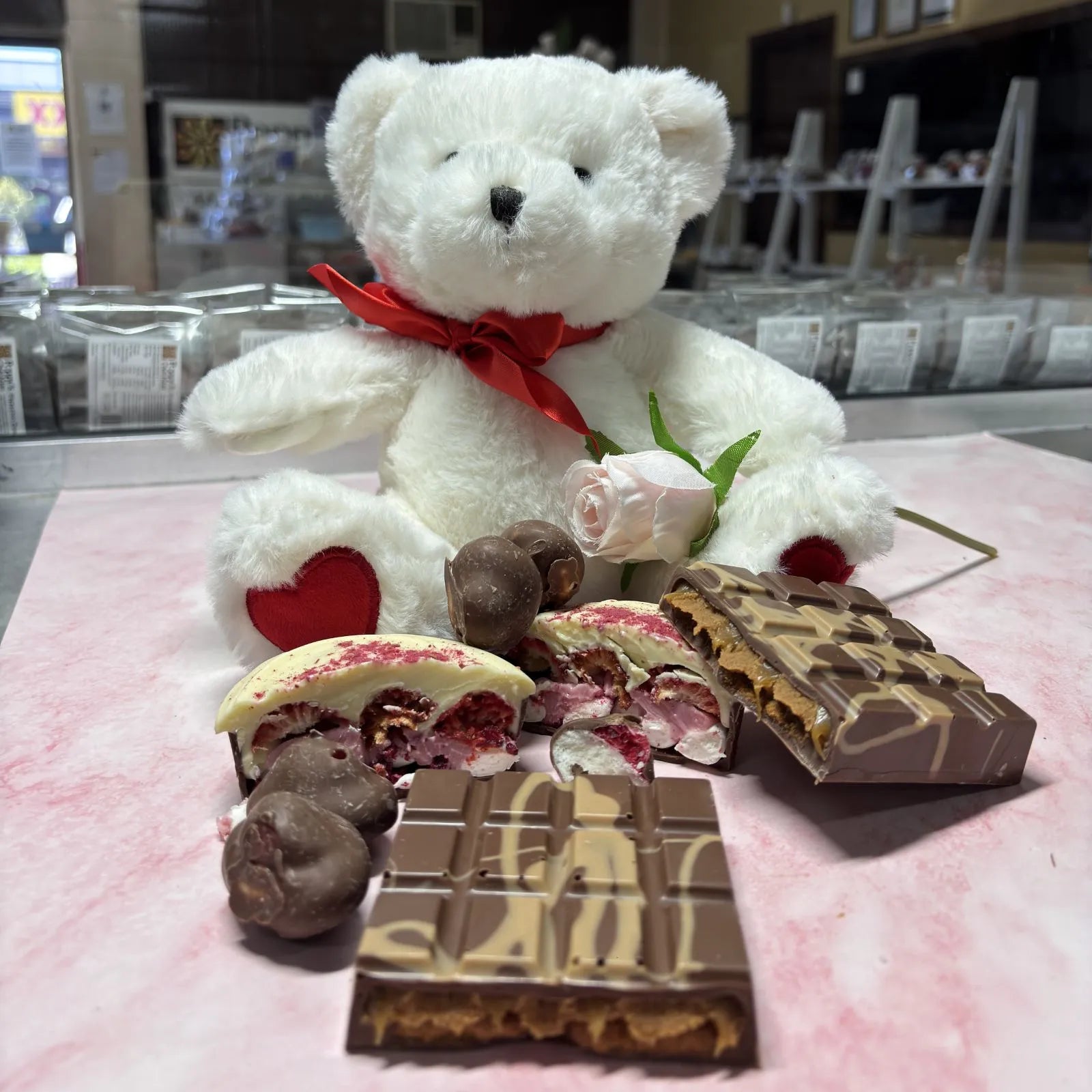 A curated Just Because hamper featuring assorted chocolates and sweets, paired with a short stem rose and a small plush love bear.