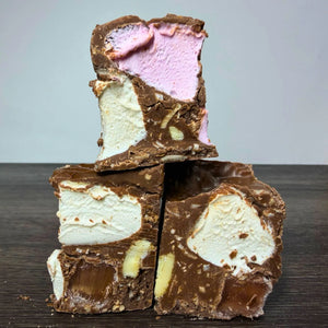 Three stacked pieces of chocolate malt candy bar with white and pink marshmallow swirls, set on a dark wooden surface against a light gray background.