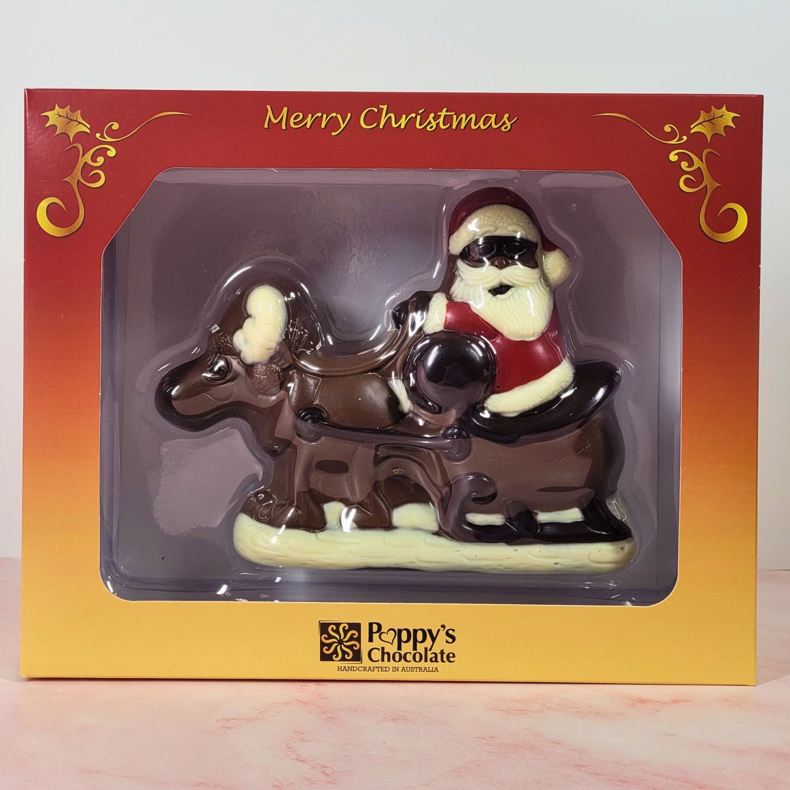Milk chocolate Santa with a reindeer and sleigh, displayed in front of its red and gold Christmas gift box.