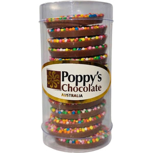 A clear cylindrical plastic container holding stacked chocolate-covered cookies topped with colorful round sprinkles. The front label reads 'Poppy's Chocolate Australia'.